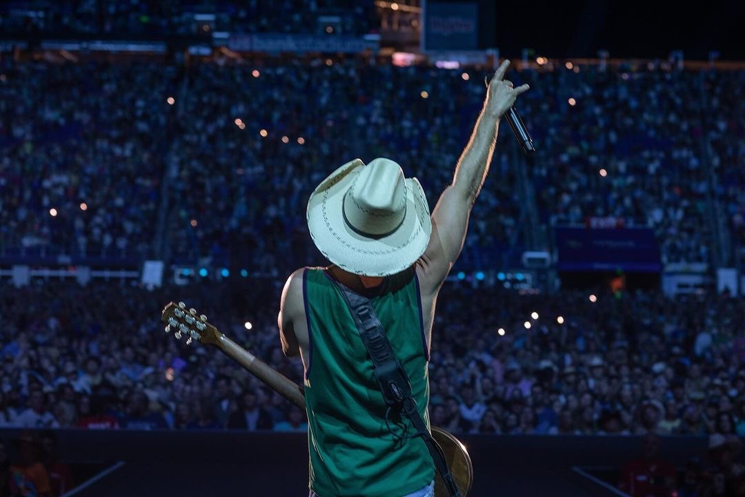 Kenny Chesney facing a stadium crowd with his hand raised
